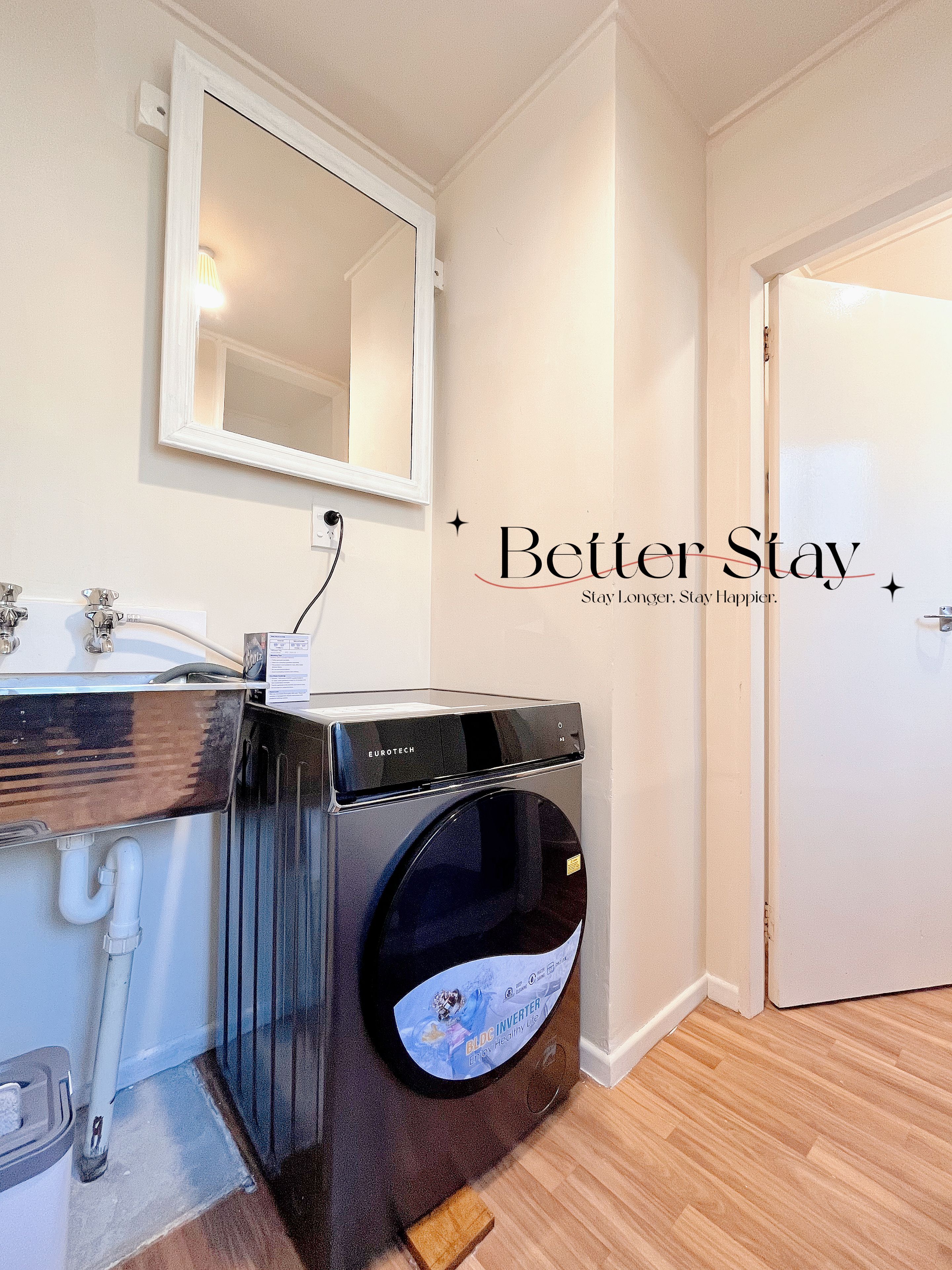 A compact room with a washing machine, a sink, a mirror, and a door.