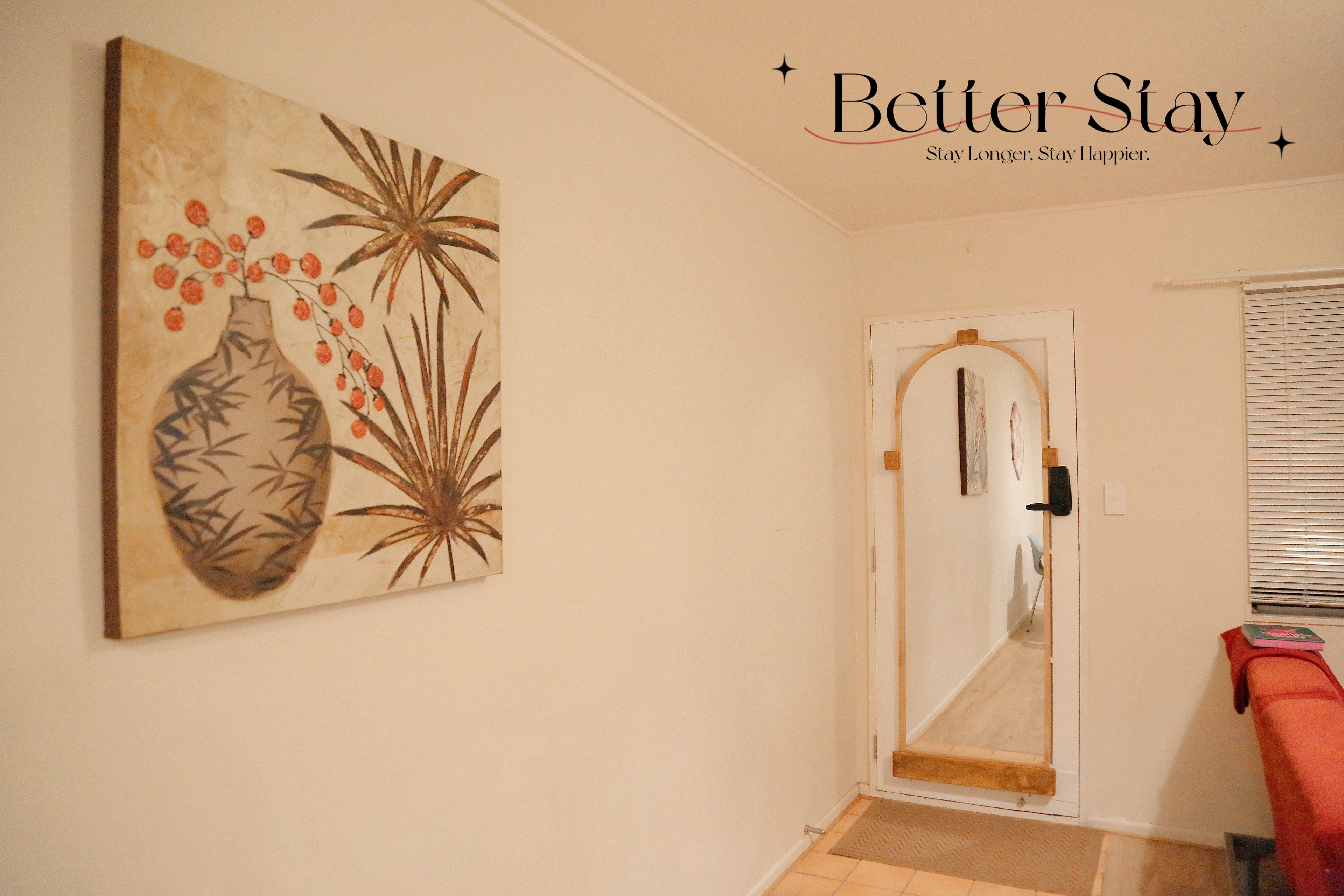 A hallway with a painting on the wall, a door with a mirror, and a window with blinds.