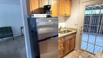 A kitchen with wooden cabinets, a stainless steel refrigerator, a granite countertop, and a sliding glass door leading to a patio.