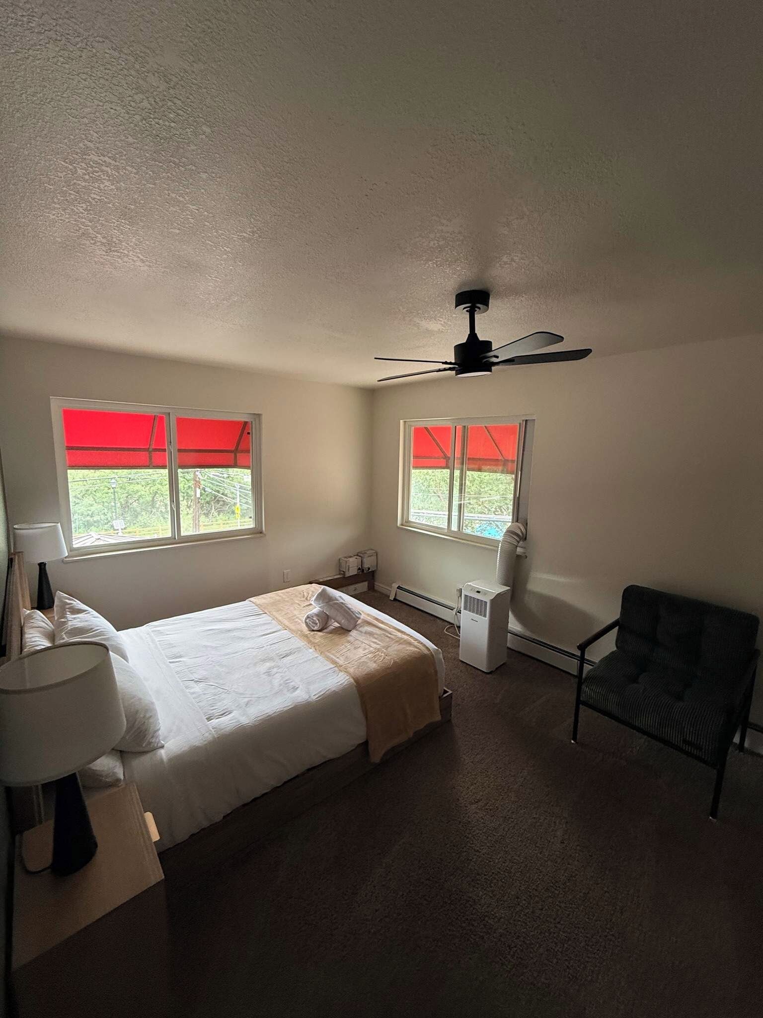 A bedroom with a bed, a chair, a heater, and a ceiling fan.