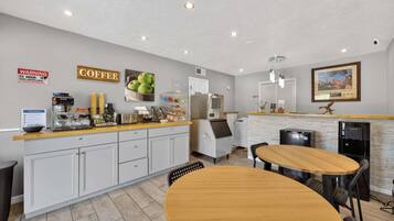 A modern kitchen with a coffee station, a dining area with a wooden table, and a refrigerator.