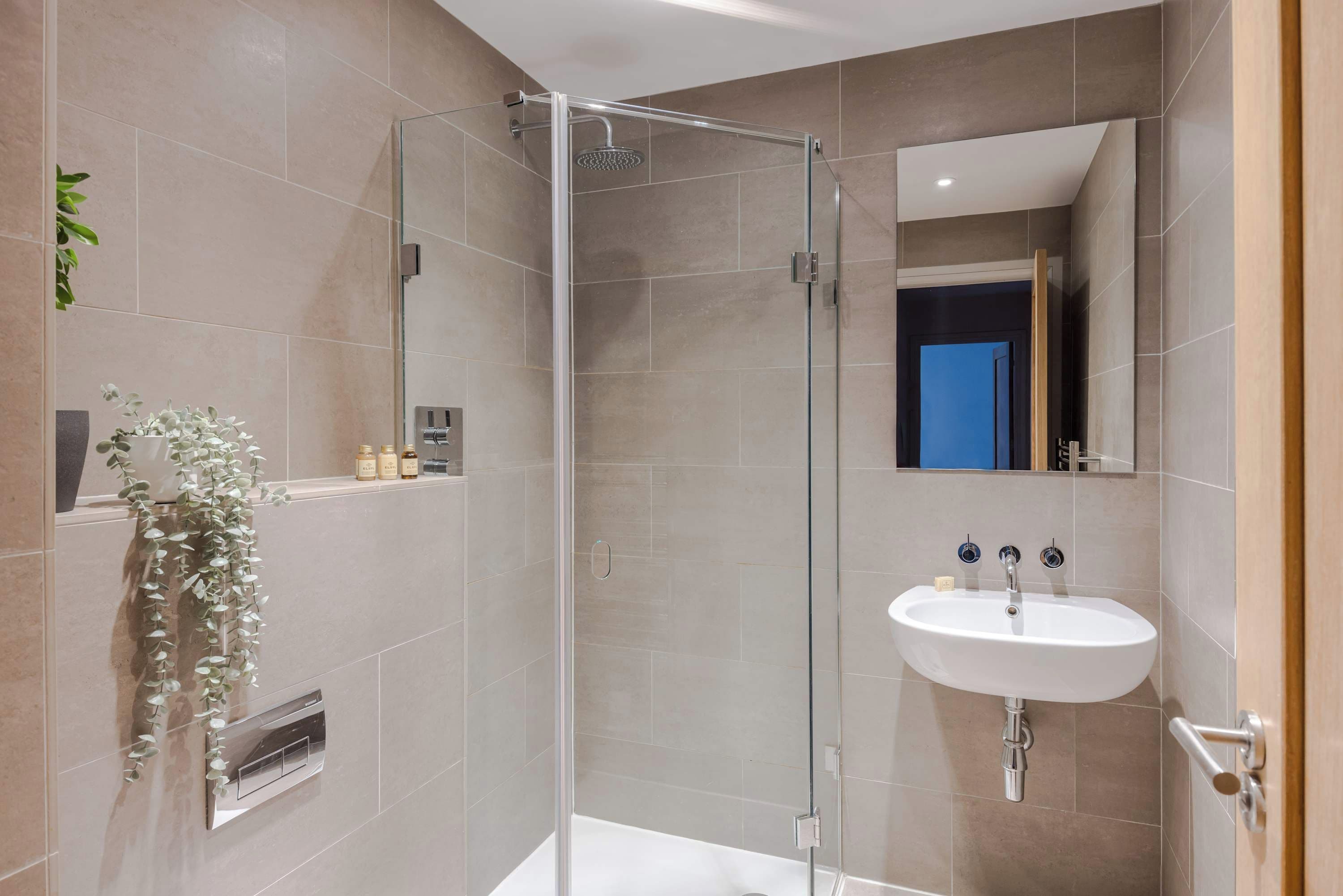 Een moderne badkamer met een douchecabine van glas, een wit wastafelmeubel en een spiegel.