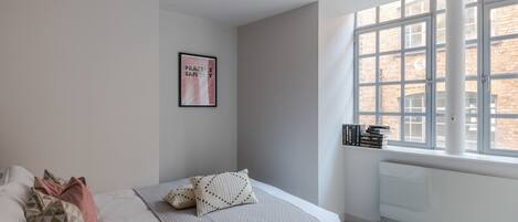 A bedroom with a bed, pillows, a framed poster, a window, and a radiator.