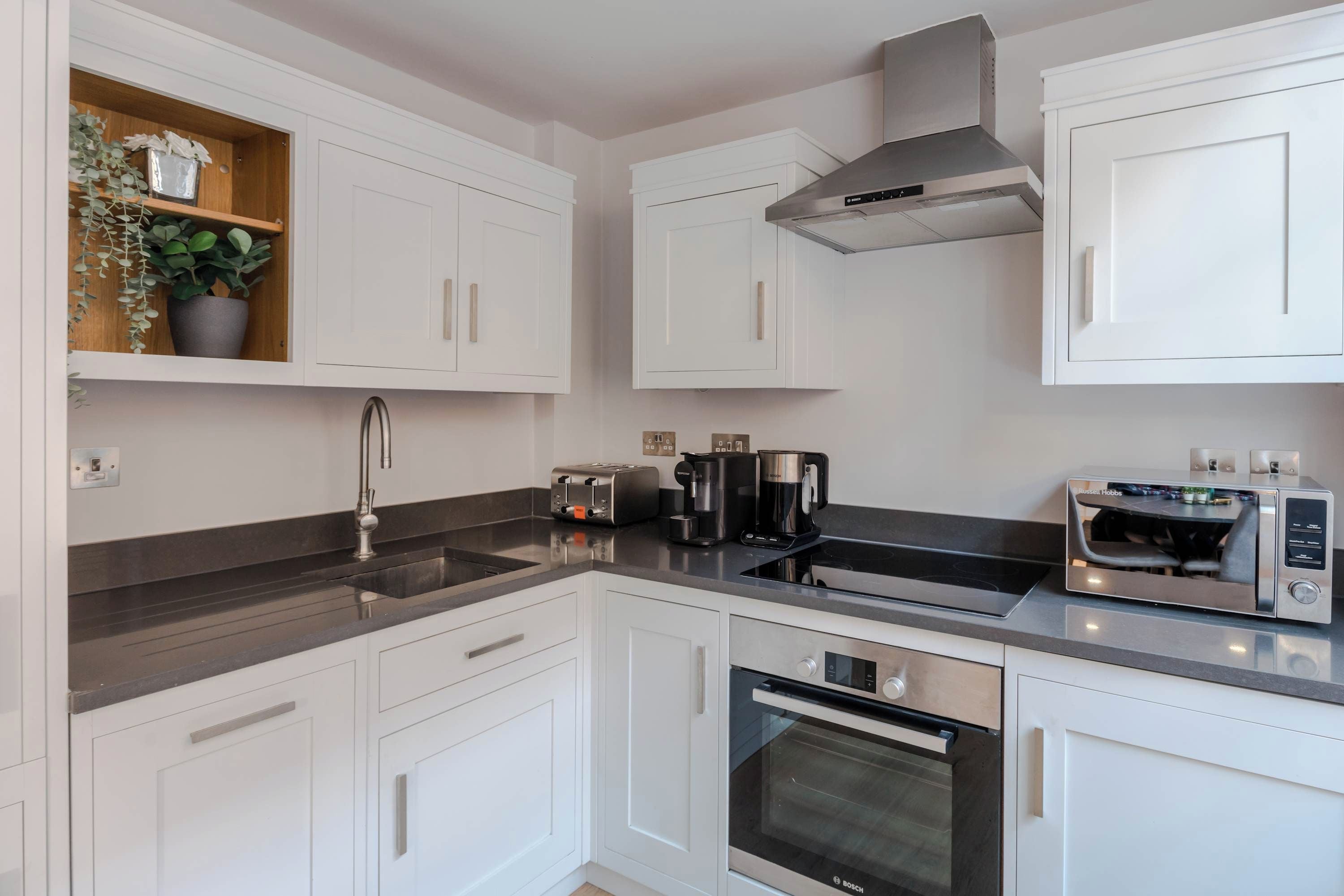 A modern kitchen with white cabinets, a stainless steel range, a Bosch oven, a coffee maker, and a toaster.