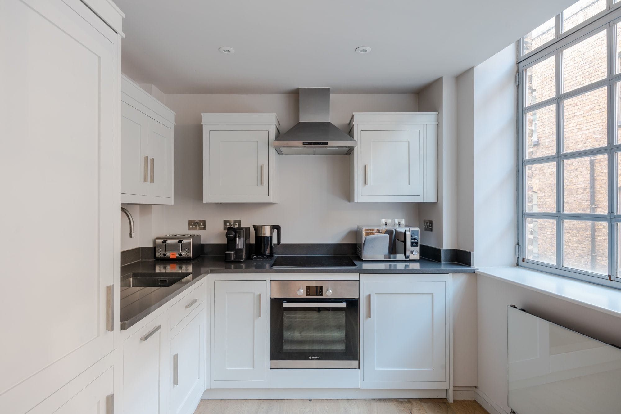 A modern kitchen with white cabinets, a Bosch oven, a toaster, and a coffee maker.
