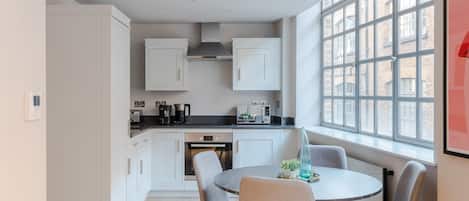 A modern kitchen with white cabinets, a black countertop, and a dining area with a round table and four chairs.