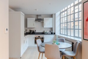A modern kitchen with white cabinets, a black countertop, and a dining area with a round table and four chairs. - The Eyre Suite Seven - Farringdon - by Frankie (London)