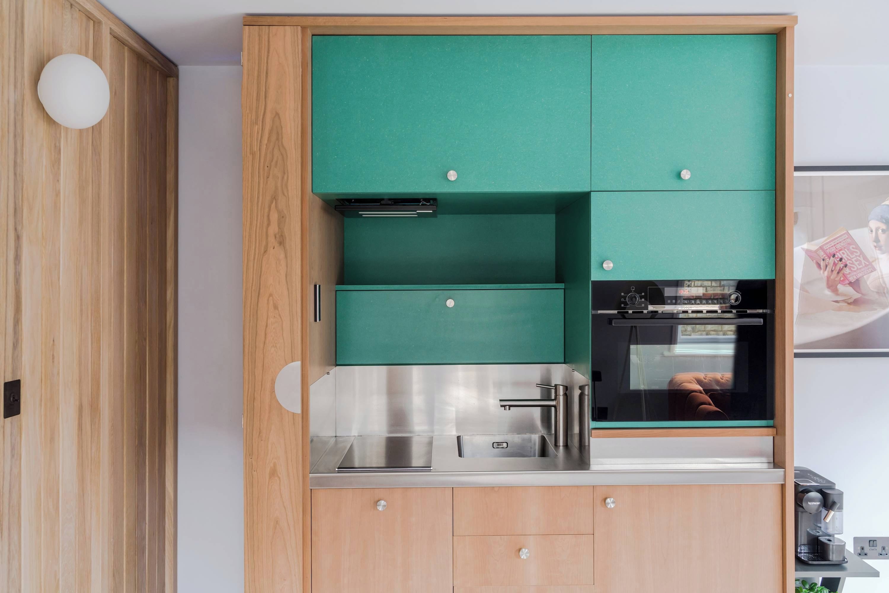 A modern kitchen with teal cabinets, stainless steel appliances, and a wooden accent wall.