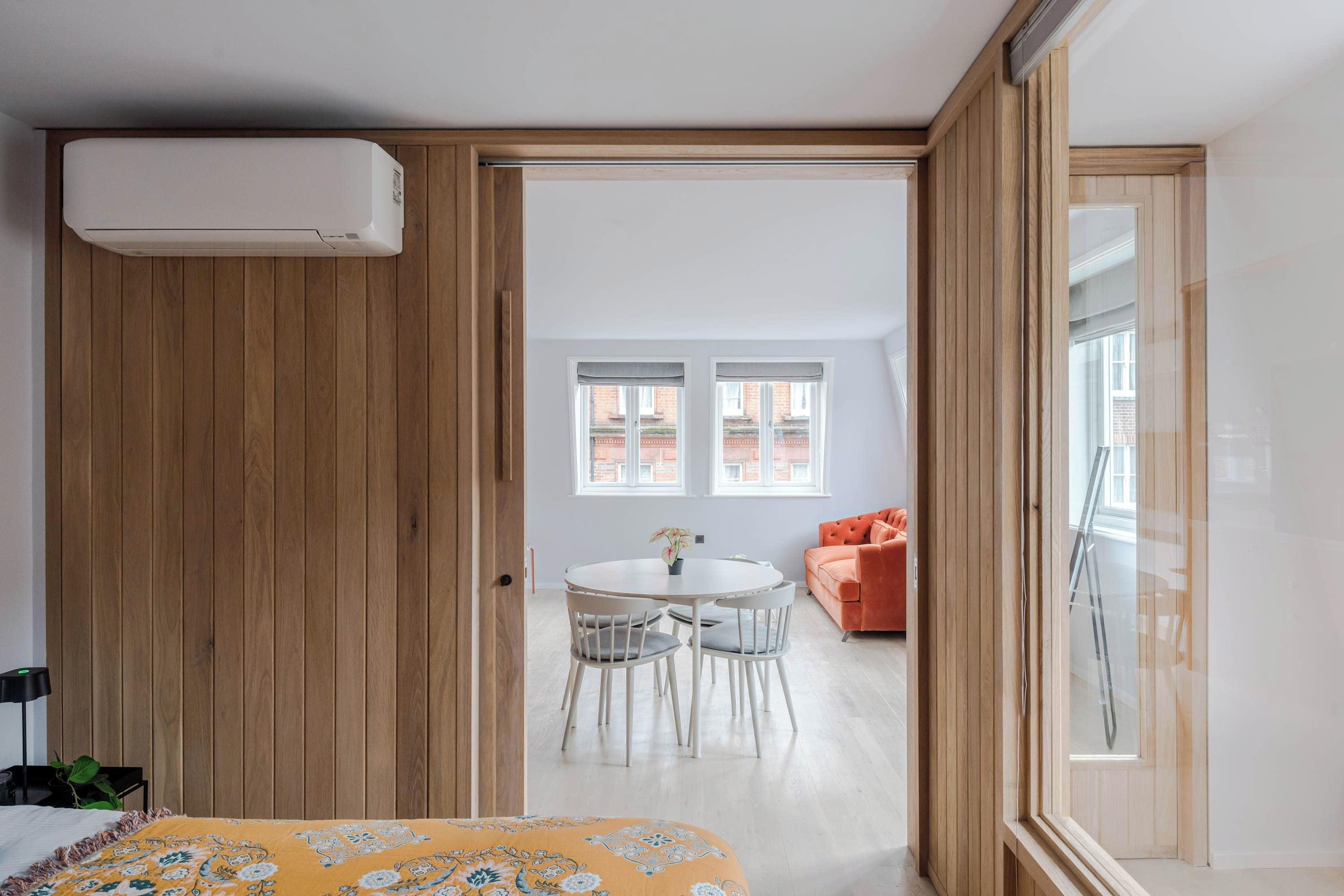 A room with a bed, a wooden wardrobe, a dining table with chairs, and a bright window.