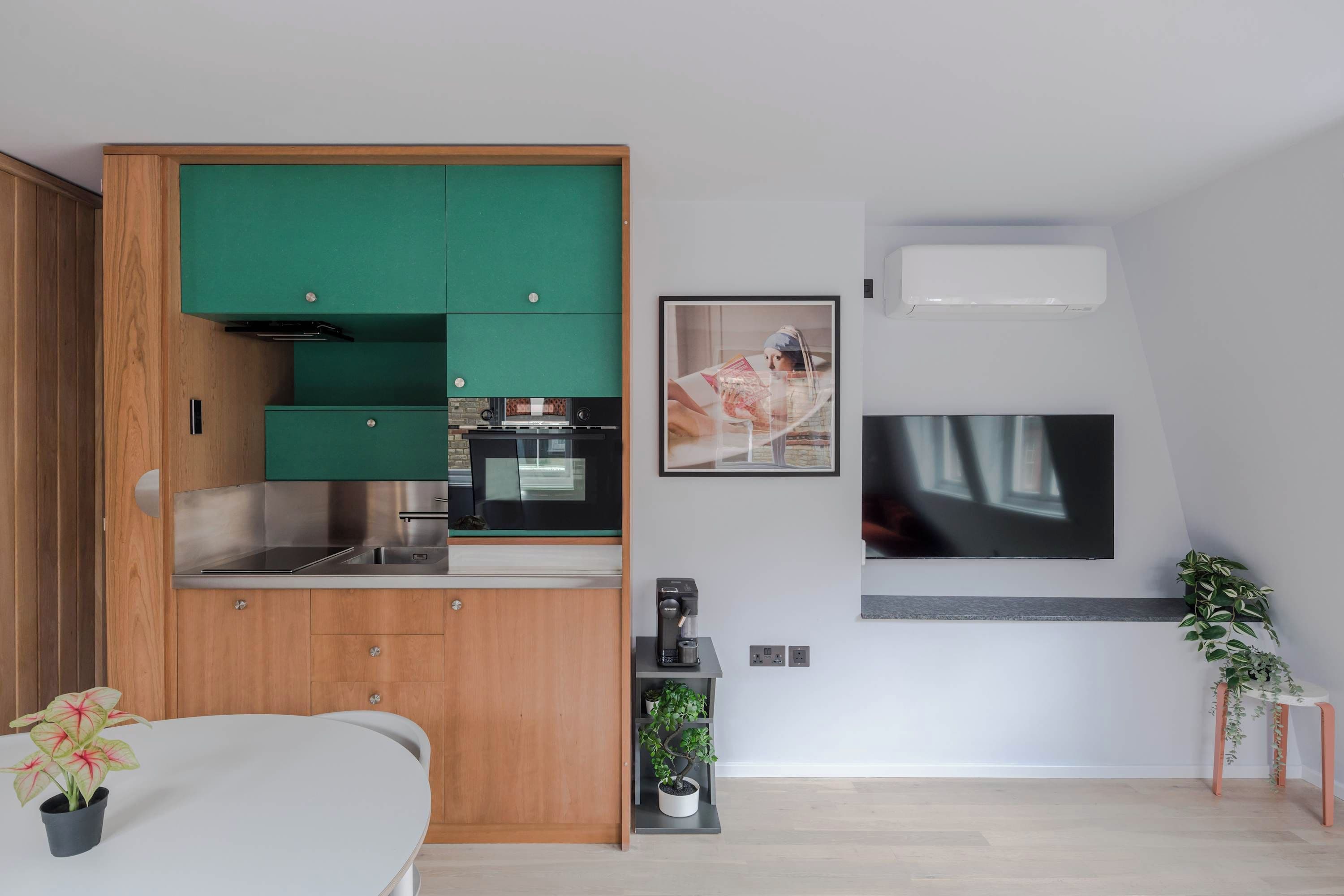 Een moderne keuken met groene kastjes, een inbouwoven en een koffieapparaat.