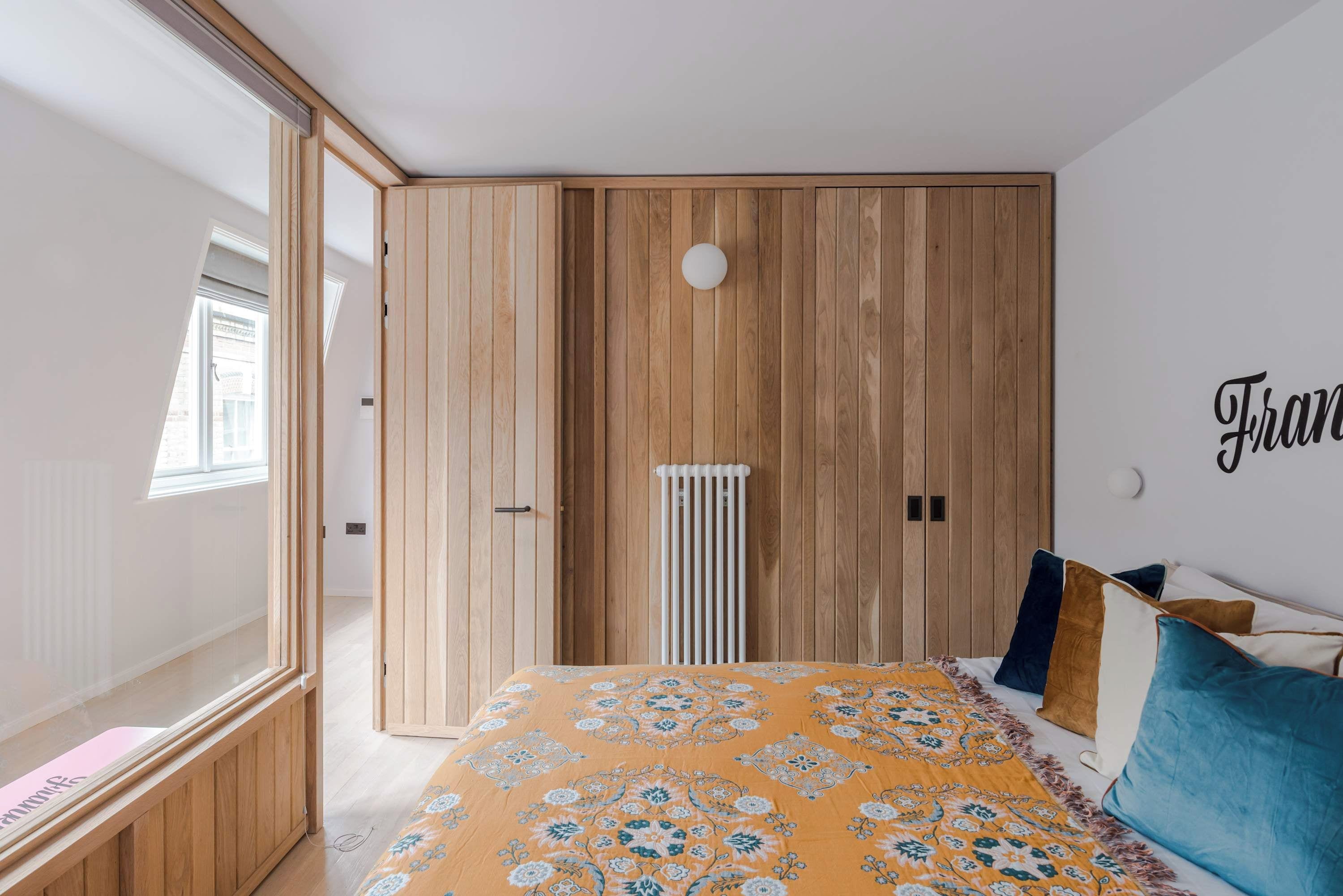 A bedroom with a wooden wardrobe, a bed with patterned bedding, and a radiator.