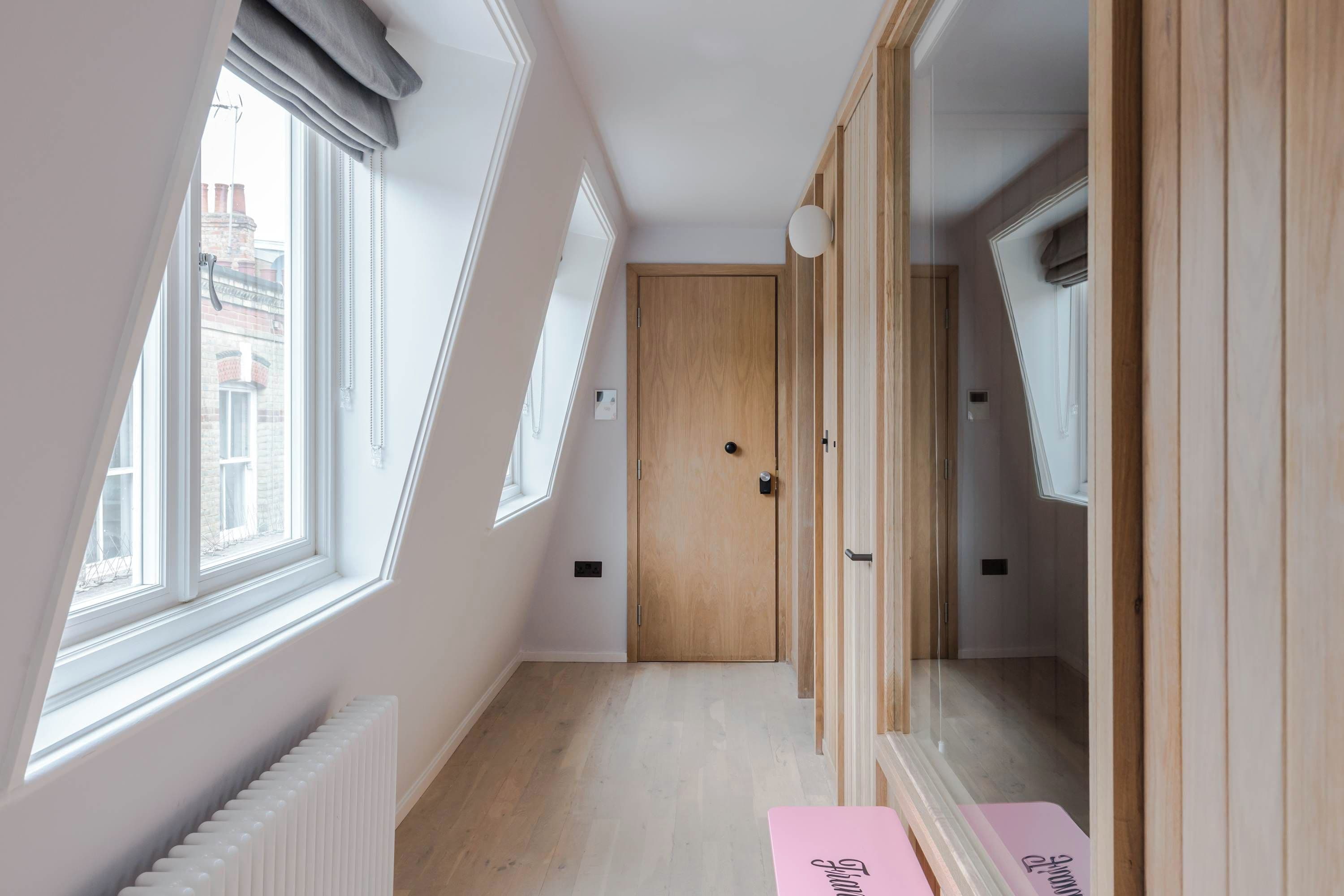 A narrow hallway with a wooden door, a radiator, and a pink bench with text.
