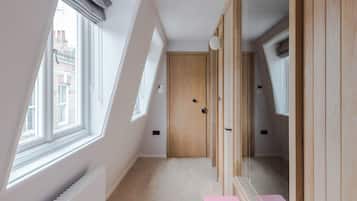Un couloir étroit avec une porte en bois, un radiateur et un banc rose orné d’une inscription.