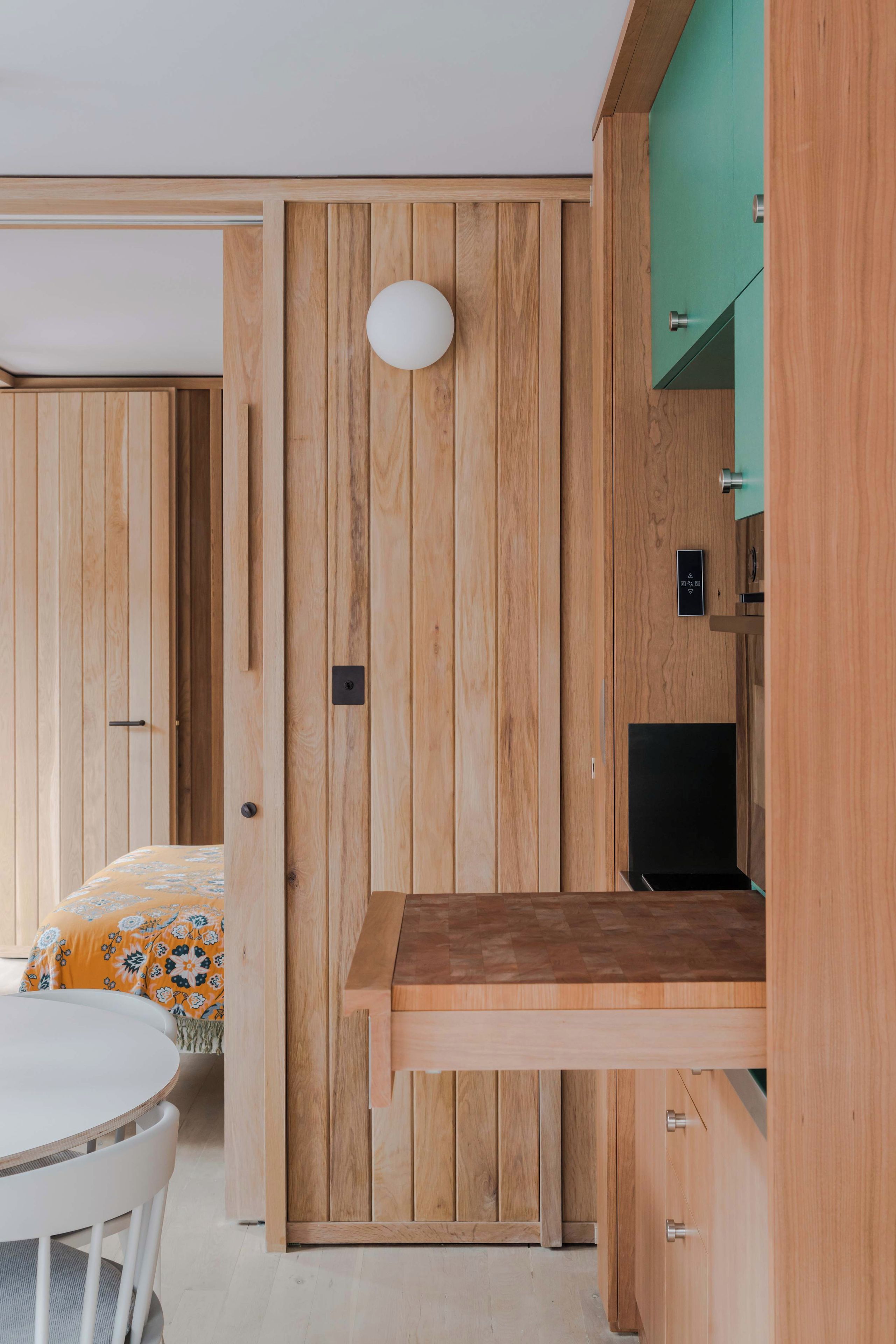 Een kamer met een houten garderobe, een bed met bloemenbedekking en een ronde tafel met stoelen.