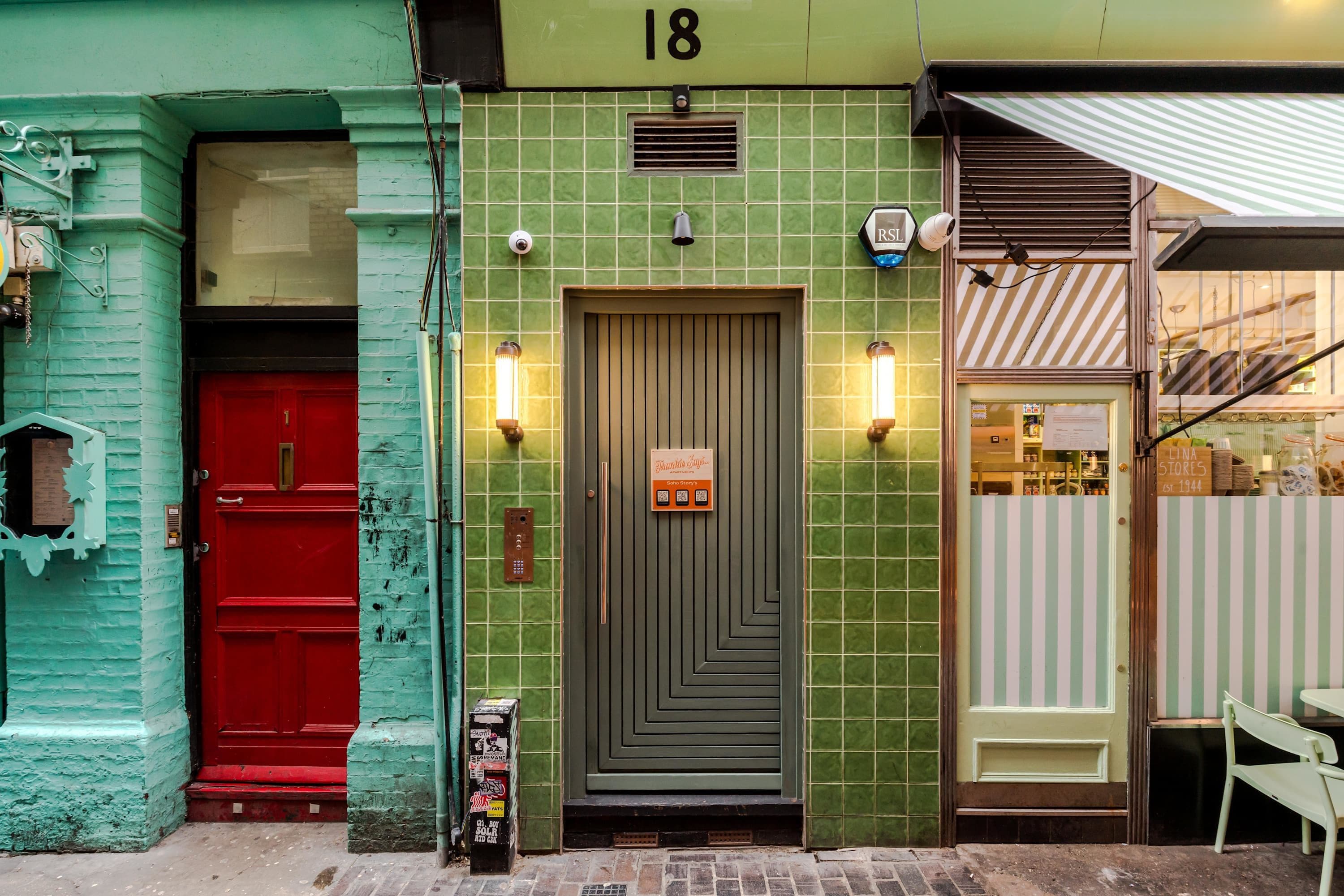 A building with a green tiled facade, a red door, and a storefront with striped awnings.