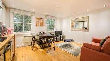 A modern kitchen with a dining area, a TV, and a large window.