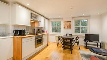 A modern kitchen with white cabinetry, a wooden countertop, and a dining area with a table and chairs.