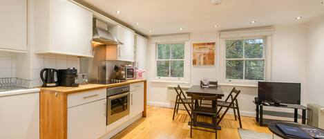 Una cocina moderna con armarios blancos, encimera de madera y un comedor con mesa y sillas.