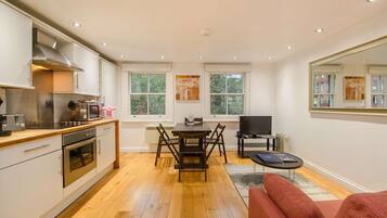 A modern kitchen with a dining area, a TV, and a sofa.