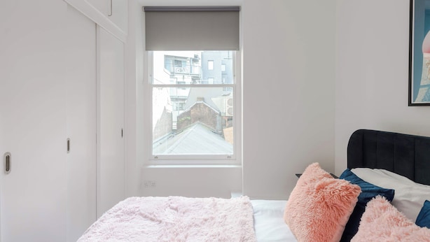 A bedroom with a bed, a window with a view of buildings, and a door to a closet. - The Foley Residence - Fitzrovia - by Frankie (London)