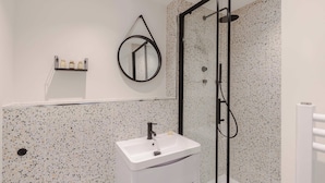 A modern bathroom with a white sink, a glass shower enclosure, and a speckled tile backsplash. - The Foley Residence - Fitzrovia - by Frankie (London)