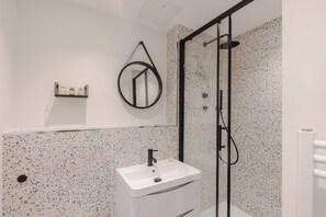 Ein modernes Badezimmer mit einem weißen Waschbecken, einer Duschkabine aus Glas und einer Rückwand mit gesprenkelten Fliesen.