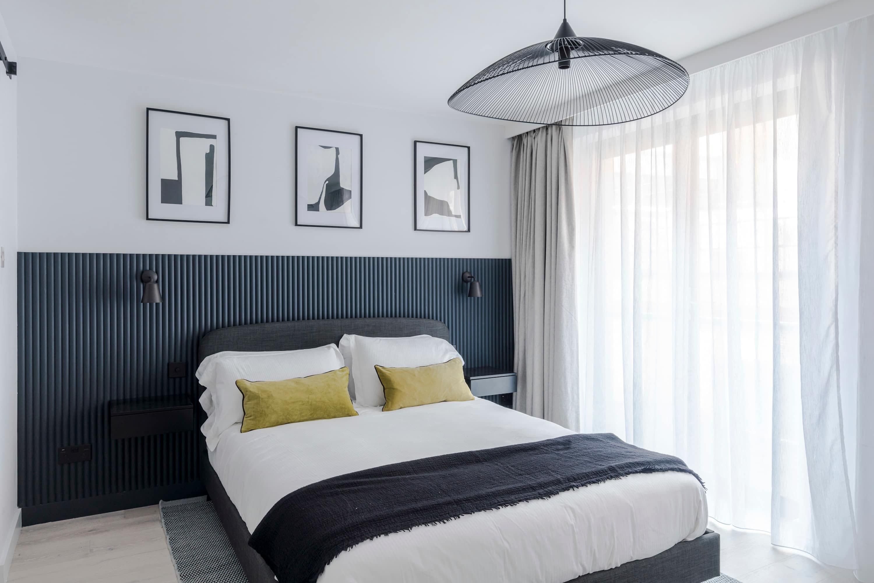 Un dormitorio moderno con una cama, mesitas de noche y un ventanal con cortinas.
