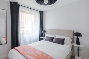 A modern hotel room with a large bed, two bedside tables with lamps, a window with sheer curtains, and a ceiling light fixture. - The Swan - Fitzrovia - by Frankie (London)