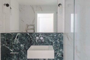 A bathroom with a white sink, marble walls, and a glass shower enclosure. - The Swan - Fitzrovia - by Frankie (London)