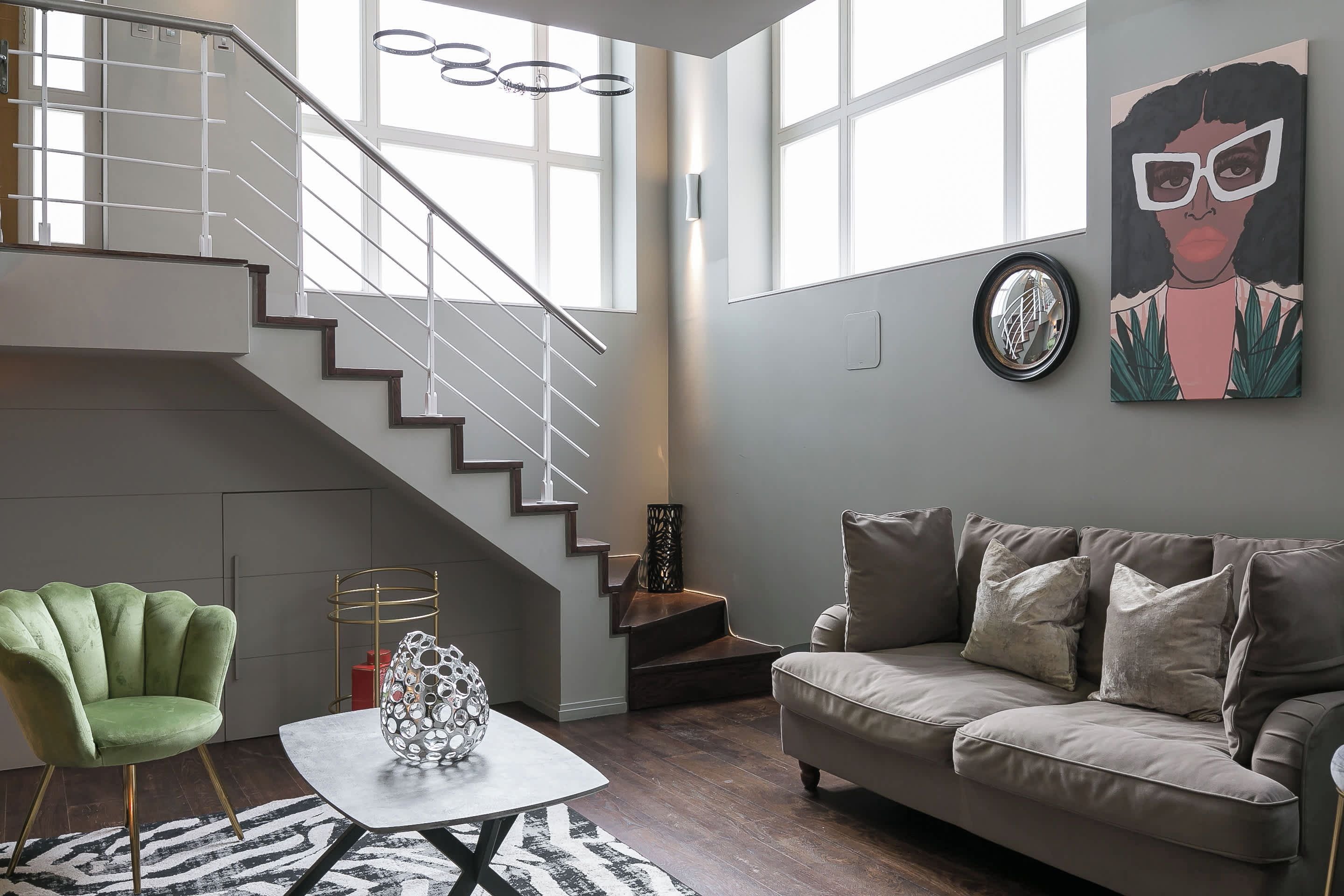 Uma sala de estar moderna com escada, uma poltrona verde, um sofá bege e uma mesa com um vaso decorativo.