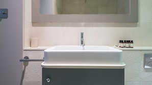 Un baño con un lavamanos blanco, un espejo encima y una repisa con artículos de tocador.