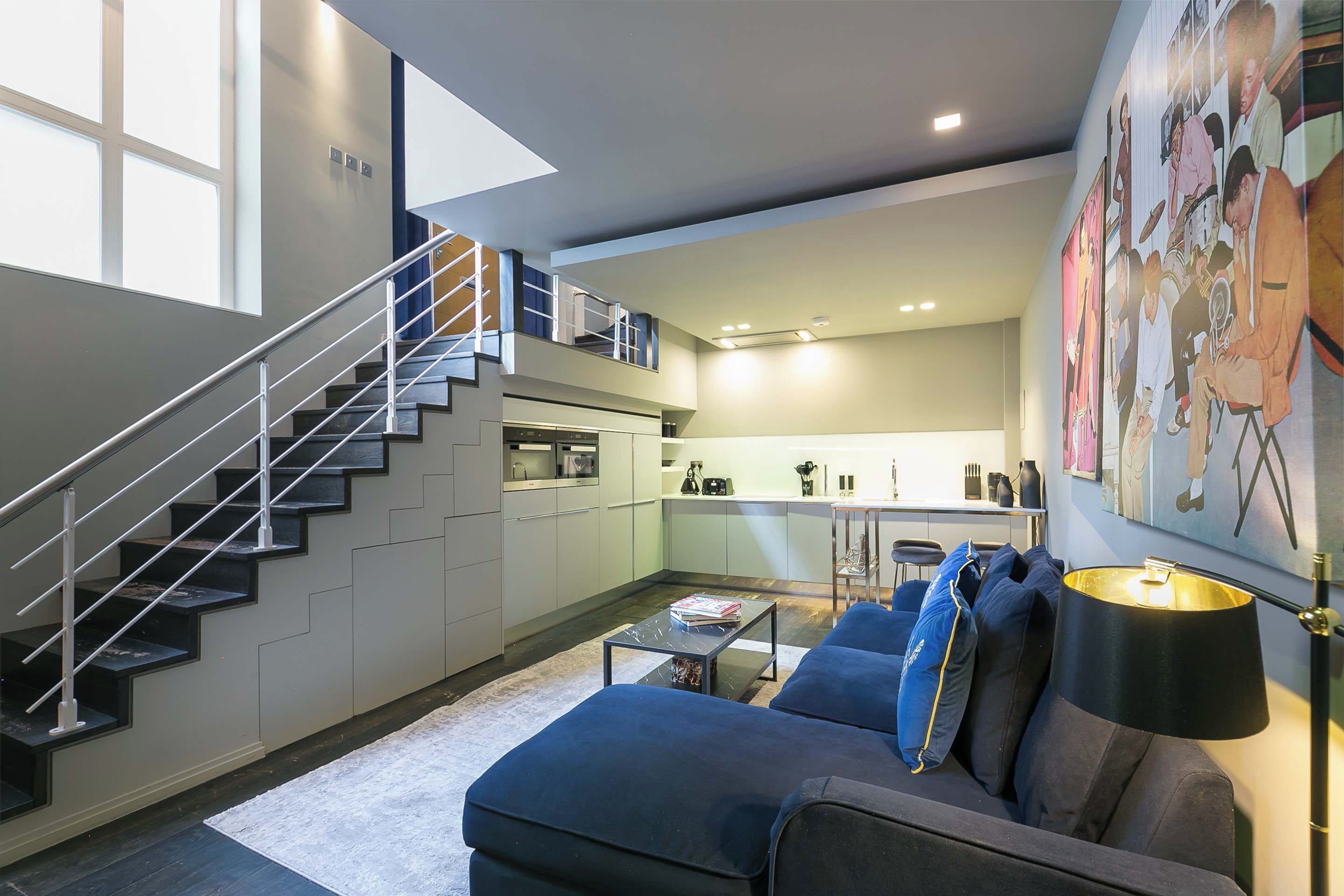 A modern interior with a staircase, a living area with a sofa, a coffee table, and a kitchen area.