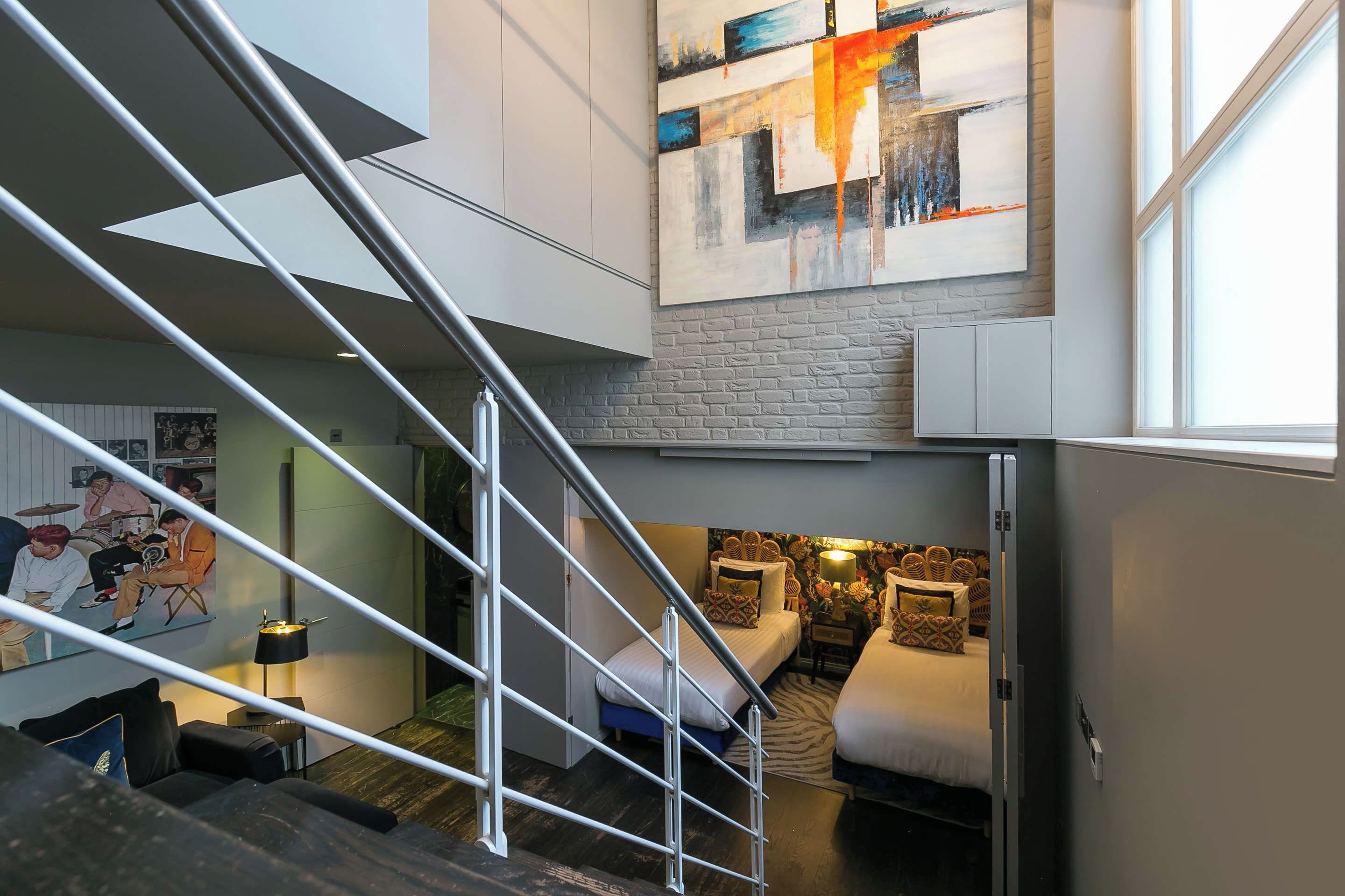 A modern interior with a staircase, a bed, a sofa, and a large abstract painting.