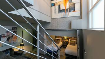 A modern interior with a staircase, a bed, a sofa, and a large abstract painting.