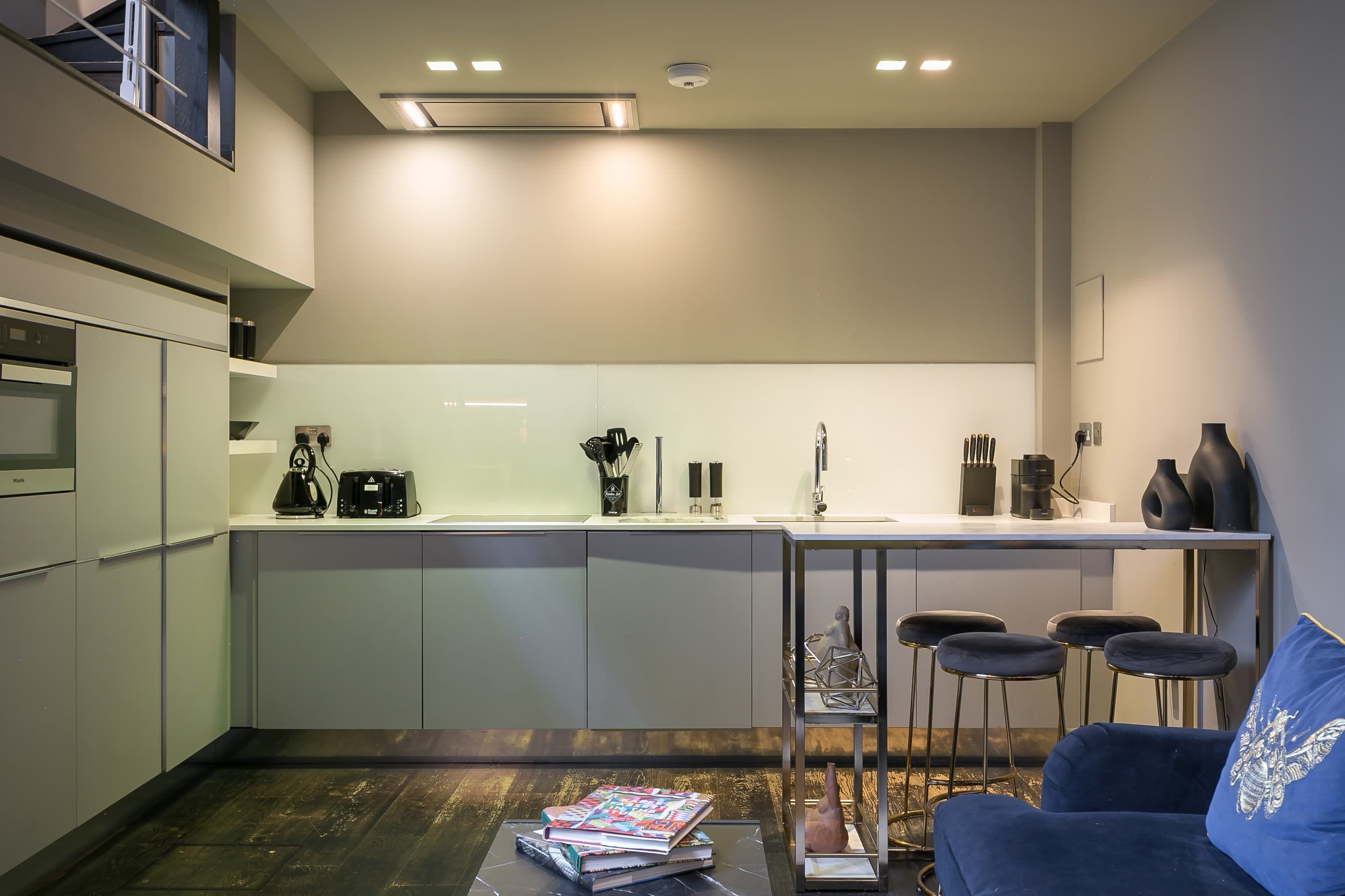A modern kitchen with a bar area, including a coffee machine, a kettle, and bar stools.