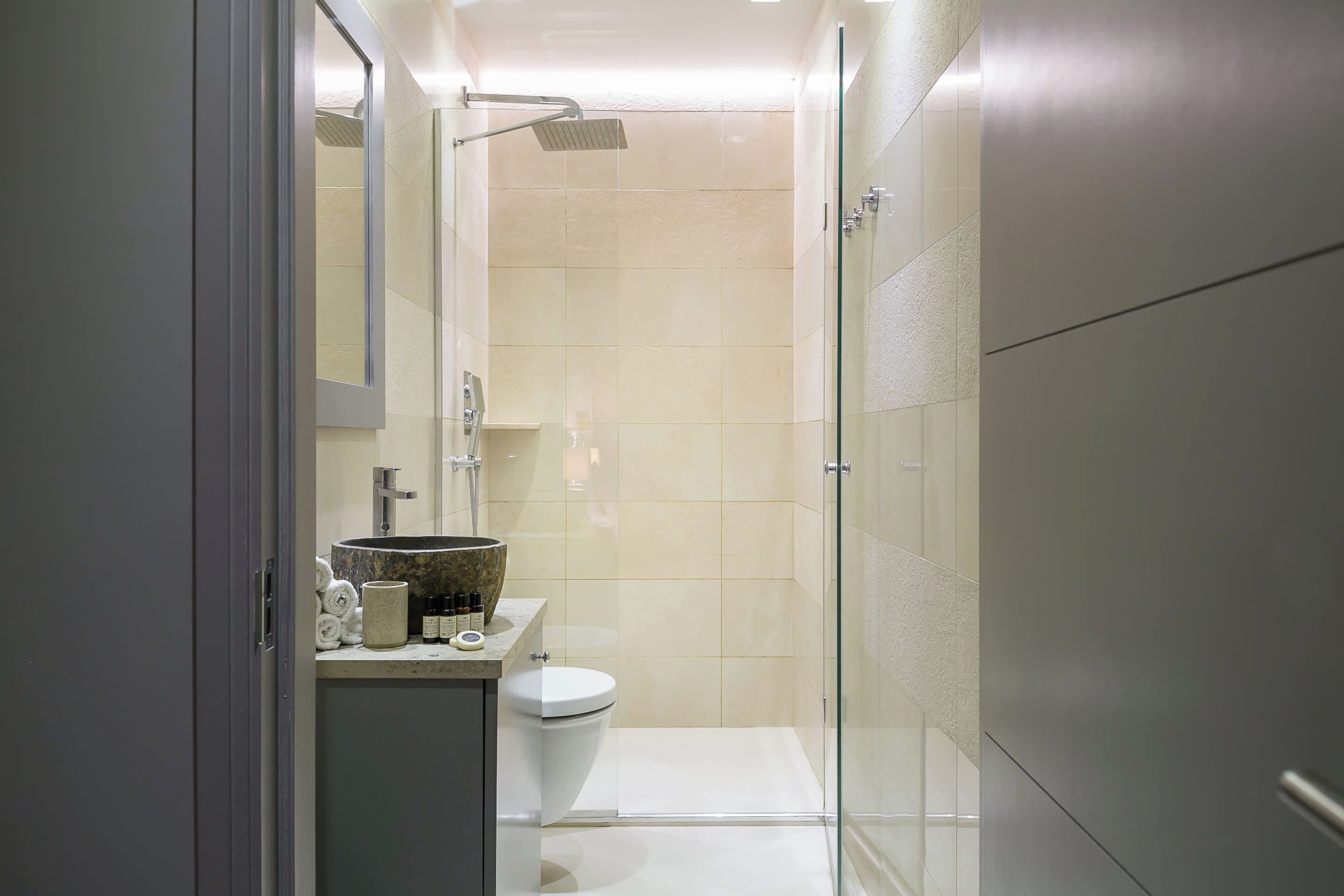 A modern bathroom with a glass shower enclosure, a toilet, and a sink with a marble basin.