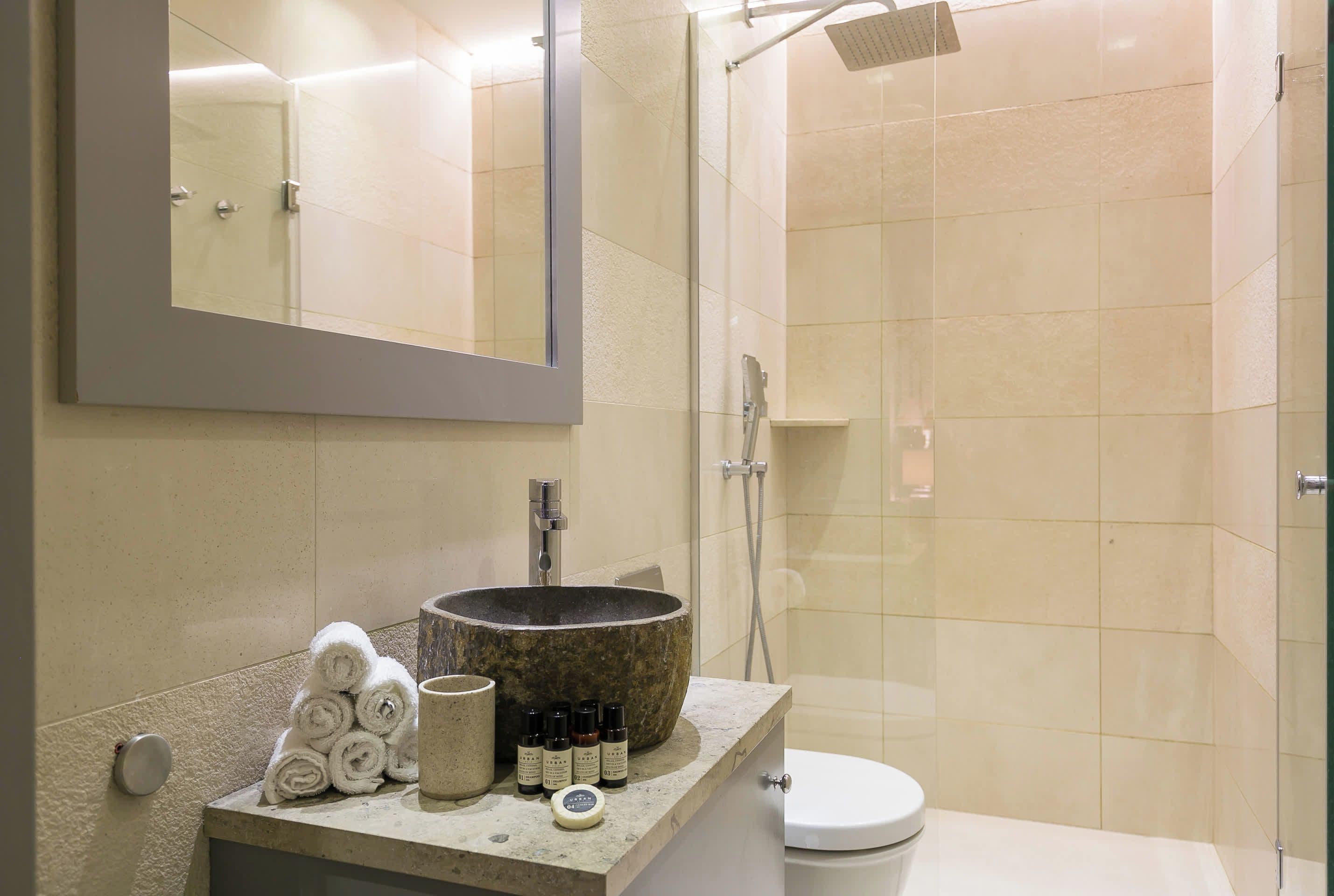 A bathroom with a stone sink, a mirror, a toilet, and a shower area.