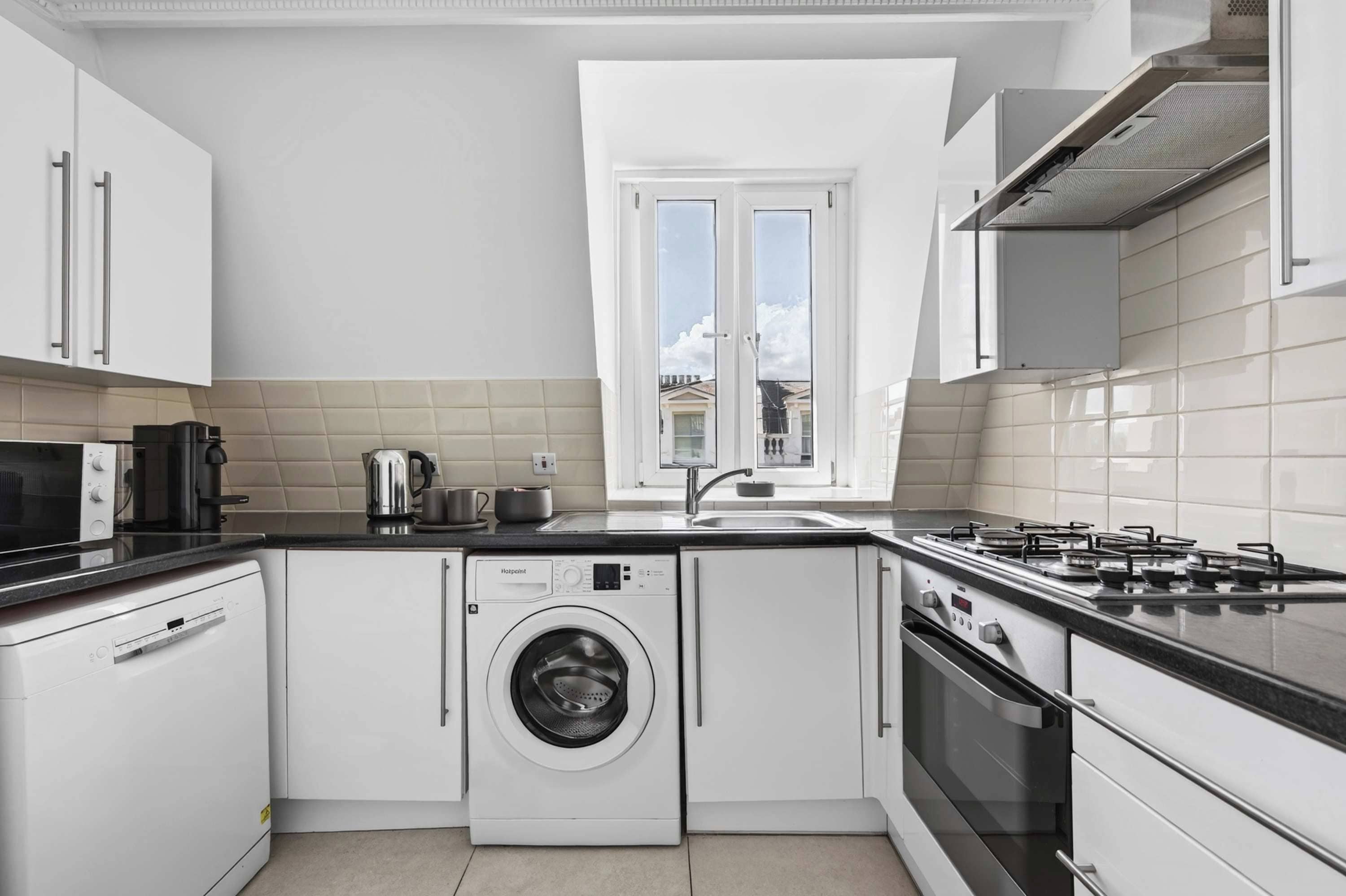 Una cocina moderna con lavadora integrada, estufa a gas y ventana con vistas a edificios.