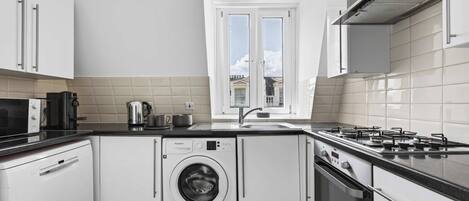 Una cocina moderna con lavadora integrada, estufa a gas y ventana con vistas a edificios.