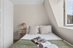 A bedroom with a bed, a nightstand, a lamp, and a window. - South Ken 2-bed - Science Museum - Lift - Sleeps 6 (London)