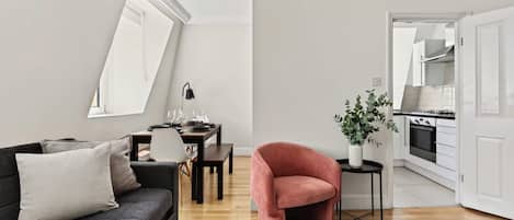 A modern living room with a sofa, a dining table set for four, and a kitchen visible through an open door.