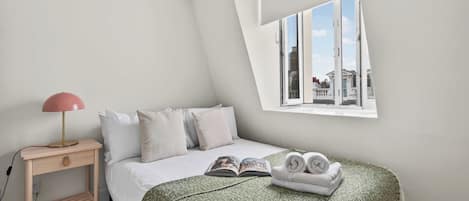 A bedroom with a bed, a bedside table with a lamp, a window with a view, and a green textured blanket.