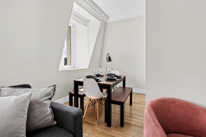 A modern living room with a dining area, a sofa, a chair, and a table set for a meal. - South Ken 2-bed - Science Museum - Lift - Sleeps 6 (London)