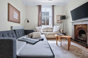 A living room with a grey sofa, a beige sofa, a fireplace, and a television. - 2-bed by Natural History Museum - Lift - Sleeps 6 (London)