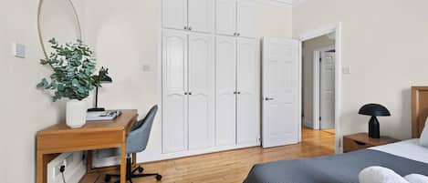 A bedroom with a bed, a desk with a chair, a wardrobe, and a plant.