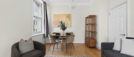 Una sala de estar moderna con un sofá, una mesa de comedor con sillas, una estantería y un ventanal grande.