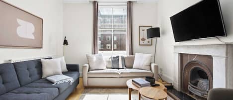 A modern living room with a sofa, a coffee table, a fireplace, and a television.