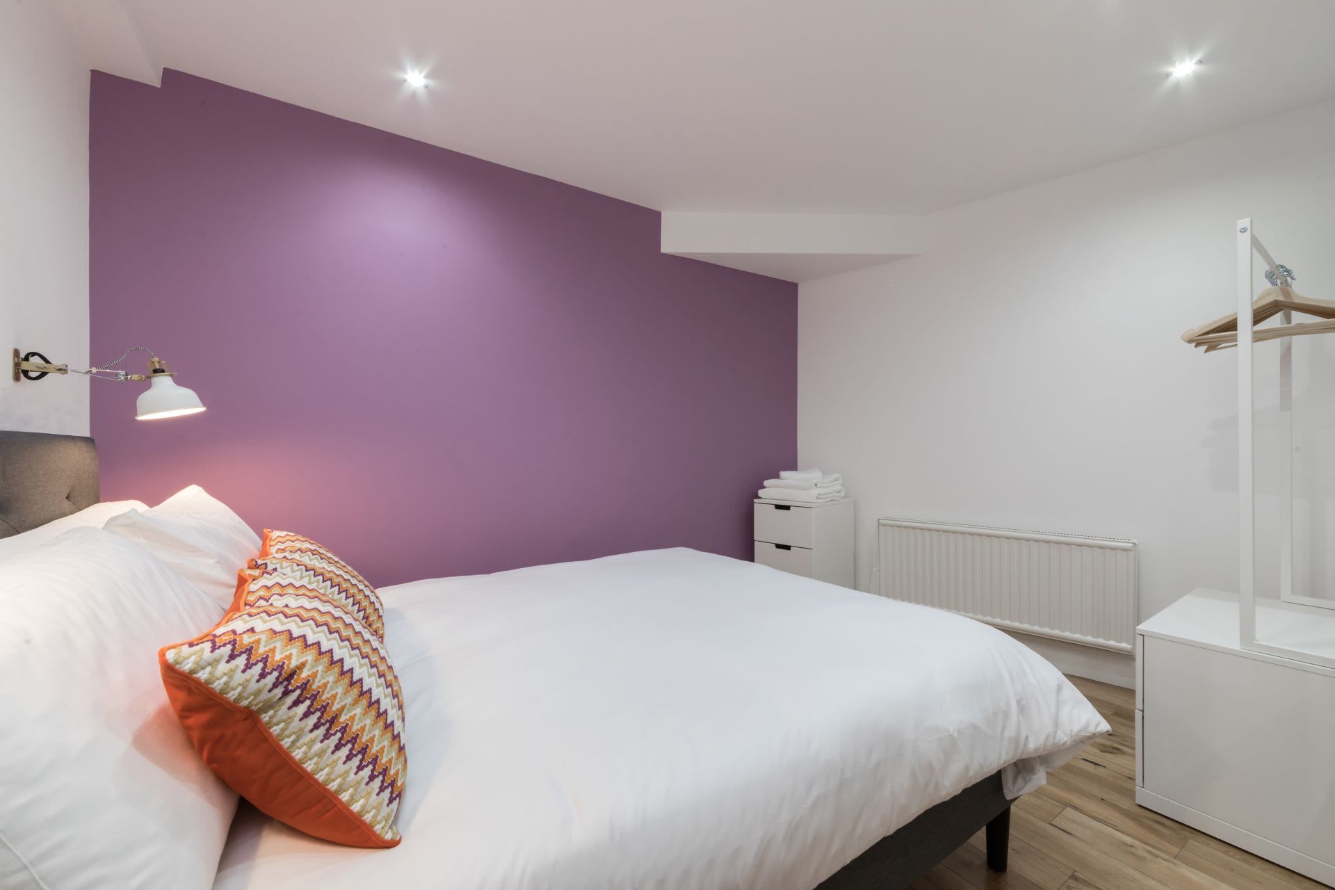 A bedroom with a bed, a bedside lamp, a radiator, and a wardrobe.