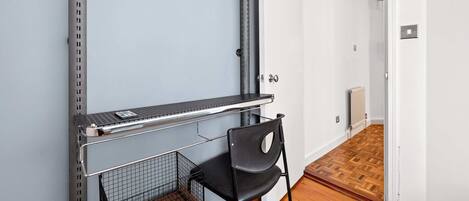 A room with a metal shelf, a black chair, a wooden floor, and a white door.