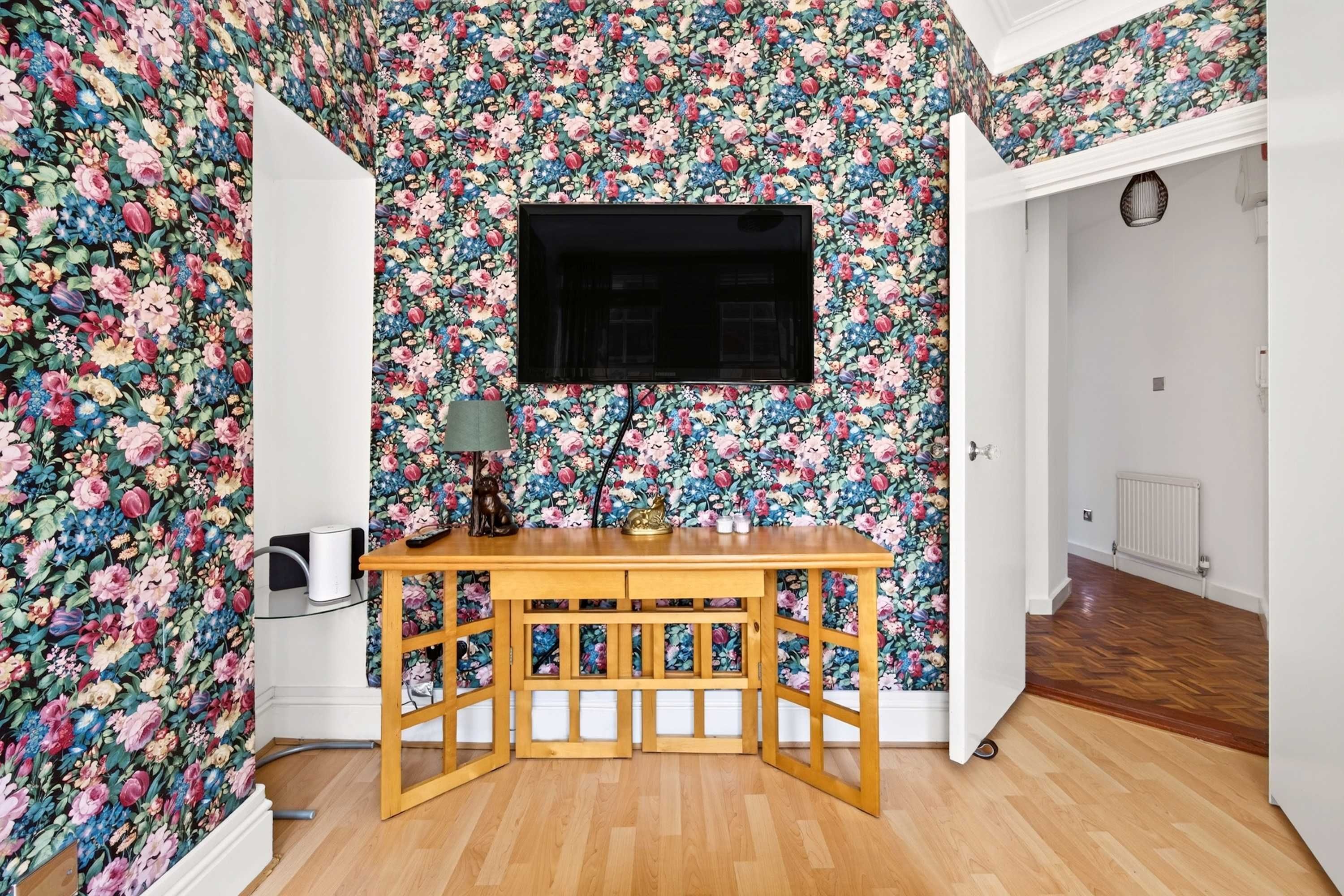 A room with floral wallpaper, a wooden table, a TV, and a radiator.